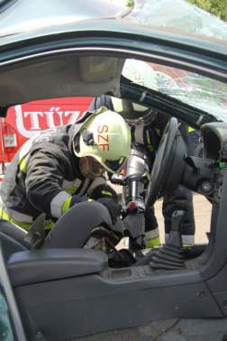 Autón keresztül fényképezve látszik két tűzoltó ahogyan dolgozik