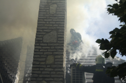 Tetőn füstben légzőben egy tűzoltó láncfűrésszel allatta egy másik tűzoltó