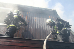 Két tűzoltó dolgozik az izzó tetőszerkezet megbontásán