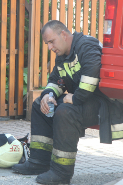 Elfáradt tűzotló vizes palackkal ül a tűzoltóautó oldalánál