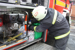 Tűzoltóautó oldalán a felszerelésekhez nyúl háttal egy tűzoltó