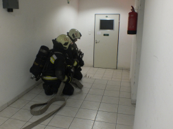 Két tűzoltó guggol a sugárral