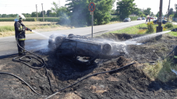 Tűzoltó vízsugárral oltja a felborult autót