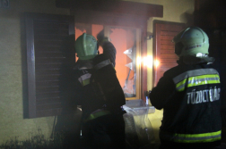 Lángoló ablak előtt háttal két tűzoltó