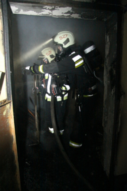 Két tűzoltó oldalról a kigyulladt melléképületben