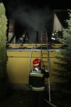 Melléképület leégett teteje és előtte háttal egy tűzoltó