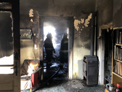 Tűzzel érintett ház szoba ajtajából látszik két tűzoltó