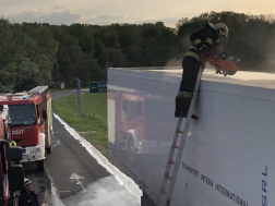Kamion tetejénél létrán roncsvágóval áll egy tűzoltó