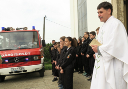 Balra tűzoltóautó jobbra a plébános középen a fiatal tűzoltók oldalról