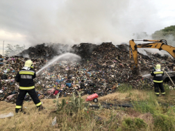 Szemétkupac előtt két oldalt tűzoltó vízzel olt